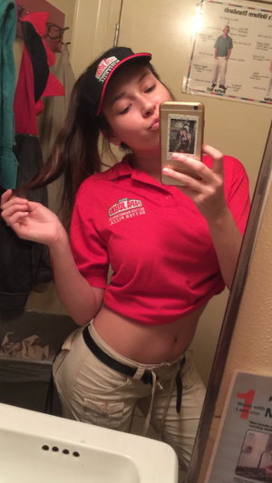 Slim woman in red polo shirt and khaki pants in bathroom mirror selfie.