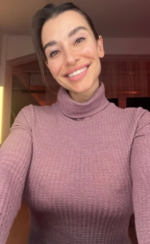 Woman in pink turtleneck sweater smiling, indoor setting, selfie.