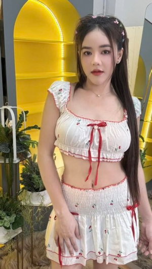 Asian woman in white cherry print crop top and skirt indoors.