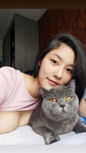 Woman in pink shirt with gray cat on bed indoors.