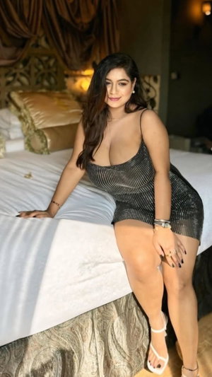 Woman in black sequined dress posing on bed in bedroom.