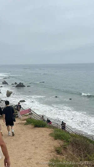 People walking along a coastal path near the ocean on an overcast day.