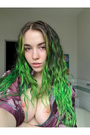 Woman with green hair in purple robe, bare chest, in bathroom.