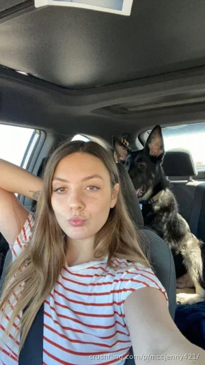 Woman with long hair in red and white striped shirt taking selfie in car with dog behind.