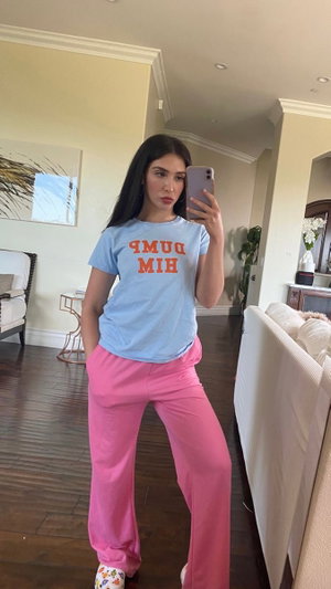 Woman taking mirror selfie in blue t-shirt and pink pants.