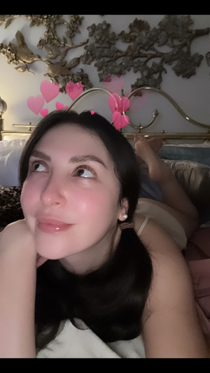 Woman with dark hair lying in bed, wearing light-colored top, pink hearts overlay.