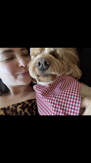 Woman in leopard print top holding dog with red checkered bandana, close-up selfie.