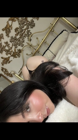 Woman with dark hair in black lingerie lying on bed with gold headboard.