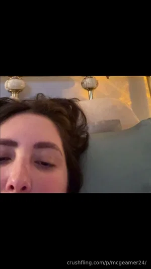 Woman with dark hair lying in bed, close-up face, bedroom setting.