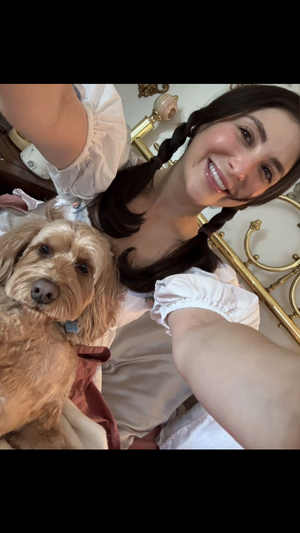 Woman with braided hair taking selfie with dog in bedroom.