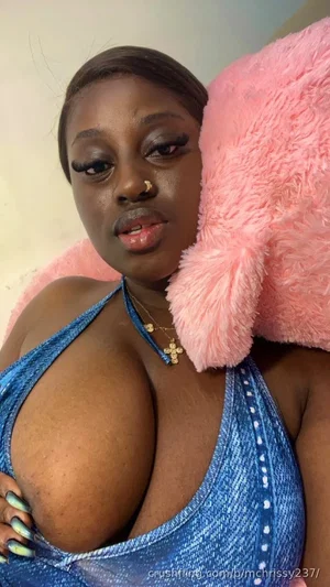 Woman in blue halter top with pink plush pillow, indoor setting.