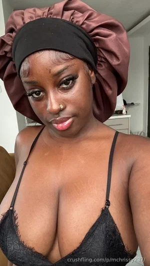 Woman with dark skin wearing black lace bra and satin bonnet, indoors.