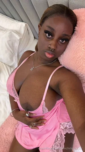 Woman in pink lace lingerie posing on bed with pink pillow, indoor setting.