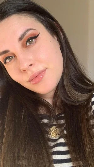 Woman with long dark hair and striped top, indoors, close-up selfie.