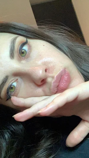 Woman with green eyes and dark hair posing close-up indoors, hand near face.