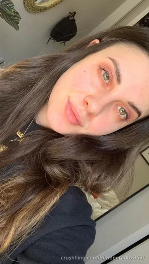 Woman with long brown hair and green eyes in a casual indoor selfie.