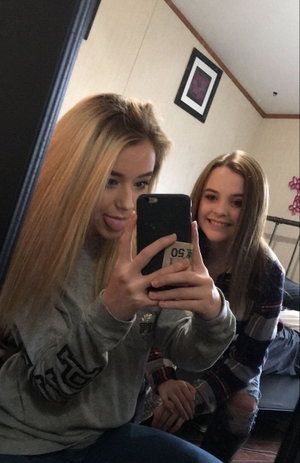 Two women in casual clothing taking a mirror selfie in a bedroom.