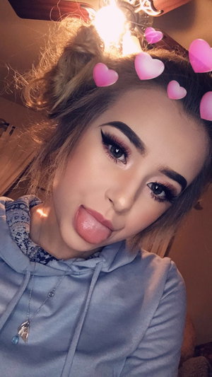 Woman with makeup and heart filters, wearing a gray hoodie indoors.