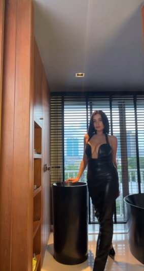 Woman in black leather dress standing in modern bathroom with large windows.