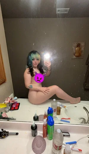 Woman with colorful hair taking mirror selfie in bathroom.