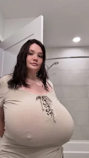 Woman with dark hair in beige ribbed top standing in bathroom.