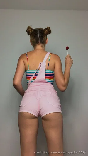 Woman in striped top and pink shorts, back view, holding lollipop, indoor setting.