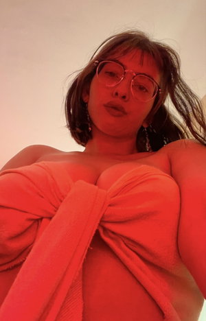 Woman with glasses wearing red towel wrap indoor selfie.