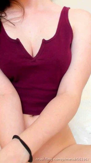 Woman in maroon tank top, sitting, legs crossed, indoor setting.