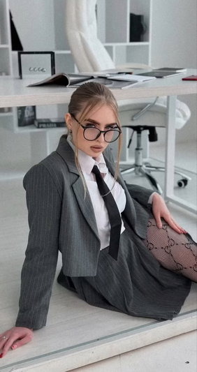 Woman in pinstripe suit and glasses sitting on floor in modern office.