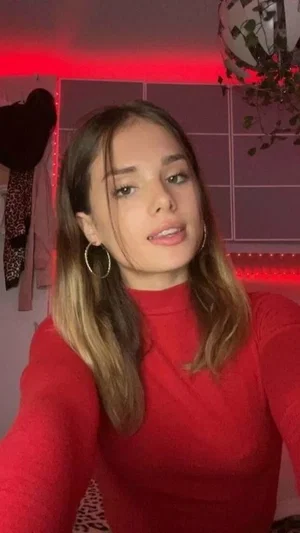 Woman in red turtleneck, indoor setting with red lighting, long hair, hoop earrings.