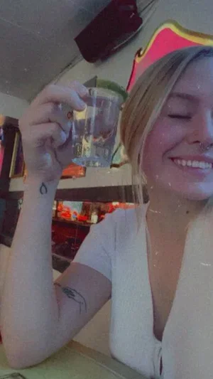 Woman with blonde hair, white top, holding glass, smiling, indoors.