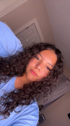 Woman with curly dark hair in blue shirt taking indoor selfie.