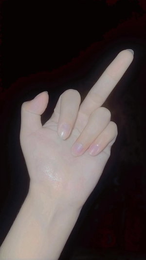 Hand with manicured nails making a finger gesture against dark background.