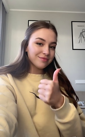 Woman with brown hair in yellow hoodie thumbs up indoors.