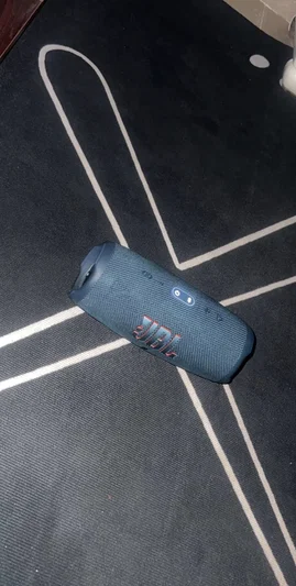 Blue JBL speaker on dark carpet with white lines.