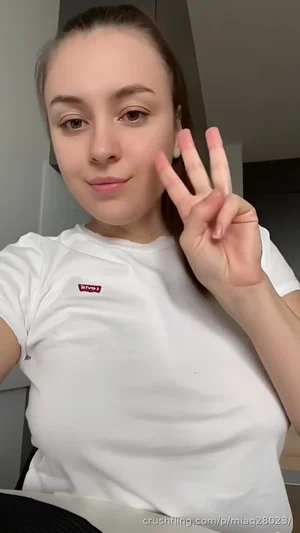 Woman in white t-shirt making peace sign indoors.