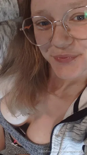 Woman with glasses, brown hair, wearing a gray top and white inner layer, indoors.