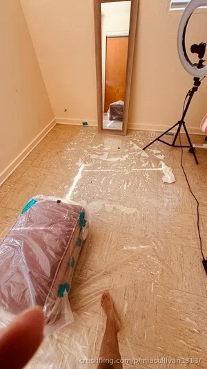Person's bare foot and hand in a room with floor protection, mirror, and ring light.