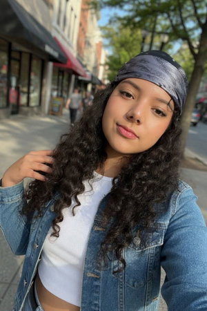 Woman with curly hair wearing white crop top and denim jacket on city sidewalk.