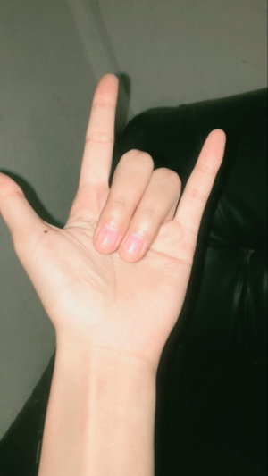 Hand making rock gesture, arm visible, dark background, indoor setting.
