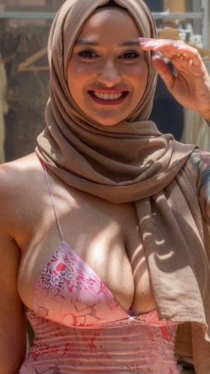 Woman in hijab and pink top smiling outdoors.