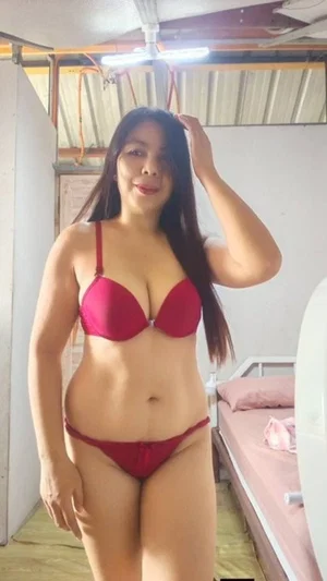 Woman in red lingerie posing in a bedroom with bed and ceiling fan visible.