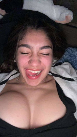 Dark-haired woman in black top lying on bed smiling.