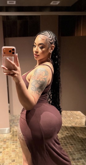 Curvy woman with braids taking mirror selfie in brown dress indoors.