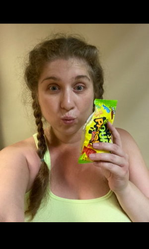 Woman with pigtails in lime tank top holds candy bag indoors.