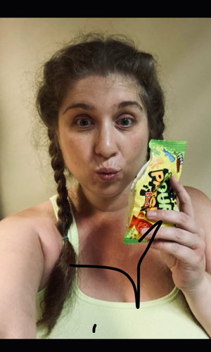 Brunette with braids in tank top holds candy bag indoors.