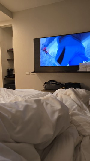 Unmade bed in hotel room with wall-mounted TV.