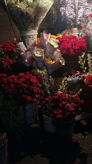 Buckets of red roses and flowers at a night market.