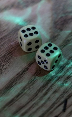 Two white dice with black dots on a wooden surface under green lighting.