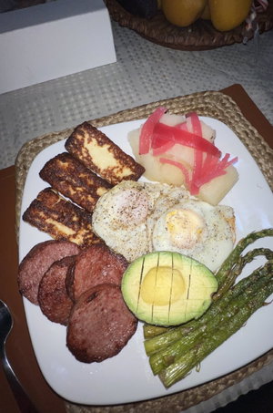 Plate of breakfast food including eggs, avocado, sausage, and hash browns on a table.